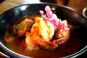 Authentic Thai Sour Curry with Shrimp and Cha-Om Omelette, Topped with Edible Flowers in Black Ceramic Bowl