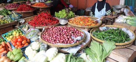 A vendor selling cooking spices such as shallots, garlic, chilies, tomatoes, and vegetables at a traditional market. Fresh and aromatic ingredients commonly used in Asian cuisine.