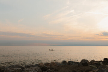 Small fishing boat sailing on calm sea at sunset with rocky coastline