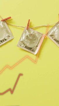Condoms hanging on string with clothespins over rising graph animation on yellow background