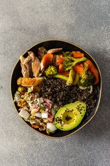 A balanced breakfast bowl with black quinoa, avocado, roast chicken, and sweet potatoes, topped with a fresh cabbage and radish salad