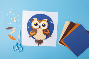 Owl made of layered paper with stars and moon on blue background. Paper craft flat lay composition...