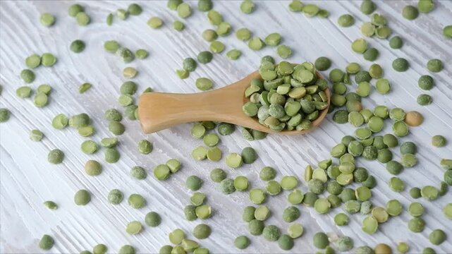 Wooden spoon with green split peas on white rustic table for cooking ingredient and vegan food concept