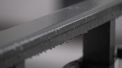 Macro view of raindrops hanging from a dark metal railing during wet weather.
