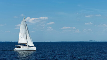 Fototapeta premium Yachting in the tropics. White sailing catamaran with raised sails moving on the sea. Sailing yacht in the ocean.