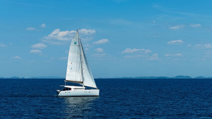 Obraz premium Yachting in the tropics. White sailing catamaran with raised sails moving on the sea. Sailing yacht in the ocean.