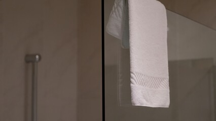 White towel hanging on glass shower partition in hotel bathroom