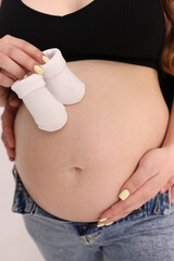 A pregnant woman holds baby clothes on her stomach. Preparation for motherhood.