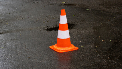 Traffic safety cone placed on a wet street after rainfall in an urban setting during morning hours