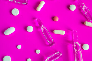 Transparent ampoules and colorful pills are scattered haphazardly on a vibrant pink background,...