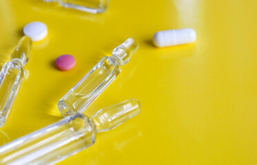 Transparent glass ampoules and colorful pills are haphazardly arranged on a bright yellow...