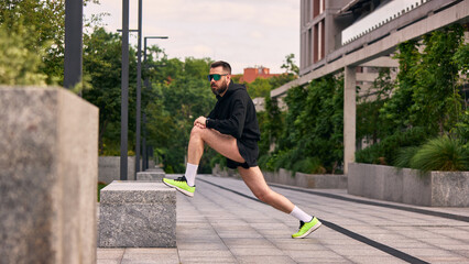 Man stretches his muscles outdoors in a city park, promoting energetic habits. Concept of urban...