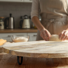 Copy space on wooden table with background of woman kneading dough on pastry board in bright home kitchen – cozy atmosphere of homemade cooking, family food and natural ingredients concept.