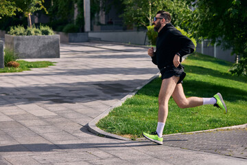 Middle aged man running along sunny park trail in athletic clothes. Concept of body strength,...