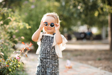 Smiling cute baby girl 2-3 year old wearing sun glasses and stylish summer clothes in park...