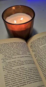 Vertical shot of a book open with a lit candle beside it.