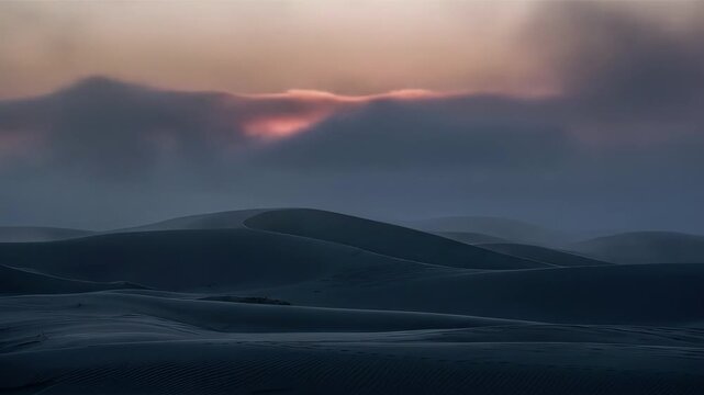 Soft colors emerge as the sun rises beyond the clouds illuminating the vast undulating sand dunes of the Sahara Desert in a mystical ambiance