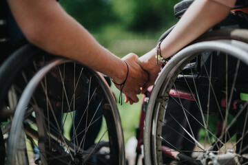 A touching moment of connectedness as two wheelchair users hold hands outdoors, showcasing mutual...