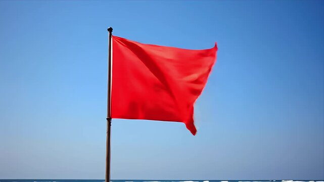 A bright red flag flutters in the wind against a clear blue sky