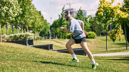 Middle aged man jogging uphill in sunny park listening to music. Concept of uphill sprint, park...