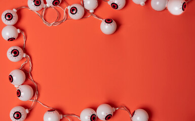 Halloween-themed eyeball string lights form a frame on a bright orange background with empty space in the center.