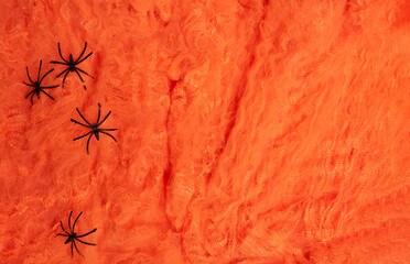 Three plastic black spiders placed on fluffy orange web-like Halloween fabric, creating a spooky...