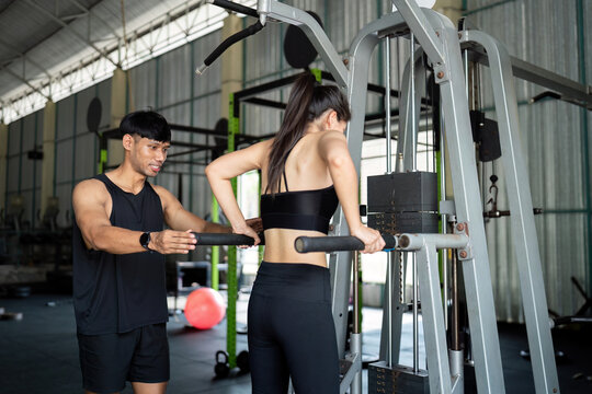 Trainer assisting woman with pull-up exercise at gym