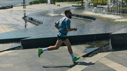 Midlife man jogging beside urban fountains on sunny day. Concept of active sprint, dynamic legs,...