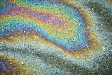 Colorful gasoline or oil spill creating a rainbow sheen on a wet asphalt surface