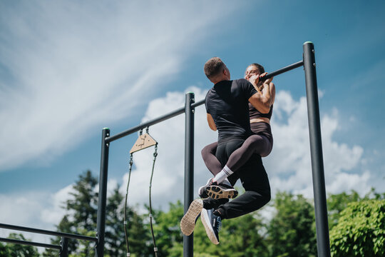 Active couple engaging in pull-ups on outdoor fitness equipment, promoting strength and motivation.