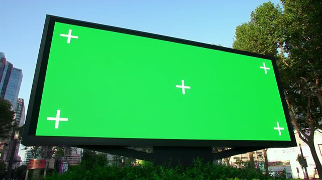 Green screen outdoor billboard with chroma key display and tracking marks in city street for advertising mockups.