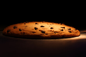 A chocolate chip cookie dramatically lit against a dark background – celebrating indulgence, nostalgia, and the power of simplicity.
