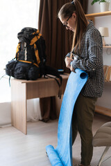 Female hiker preparing to travel packing Hiking backpack with mat to trek in mountains in home...