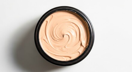 Top view of a round black container filled with creamy beige foundation with swirling texture and dark specks