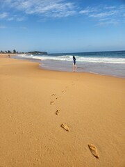 A tranquil seaside walk captured on a golden beach, where gentle waves meet the footprints of a lone figure. A peaceful video with only the sounds of the ocean breeze and footsteps in the sand.