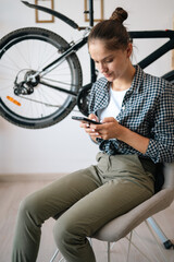 woman sitting on chair at home repairing bicycle at home reading online tips using AI assistant,...