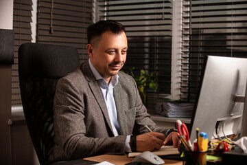 Confident businessman in a suit jacket working at a modern office desk. Sitting with a notebook and...