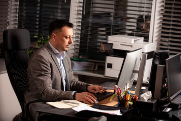 Confident businessman in a suit jacket working at a modern office desk. Sitting with a notebook and...