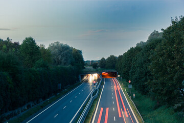 Long exposure shot of a multi-lane highway at dusk, with vibrant red light trails from vehicles moving away on the right