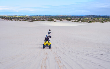 Four electric quad bikes driving in a line on white sand dunes, Atlantis, South Africa