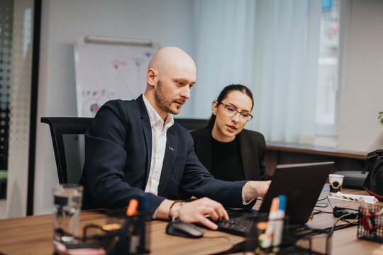 Two business people actively engaged in collaboration around a laptop, conducting a productive meeting in a bright workspace with natural lighting and modern office decor.