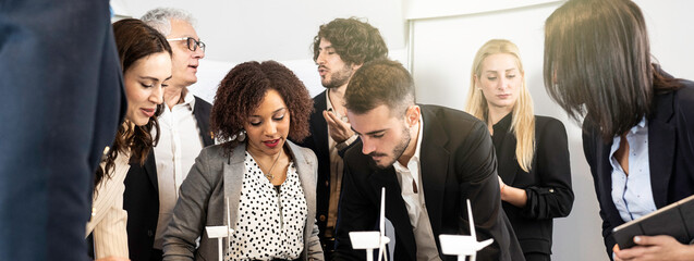 Diverse group of business professionals collaborating on wind energy models in office meeting. Multicultural team working on sustainability and innovation projects. Clean energy and teamwork concept.