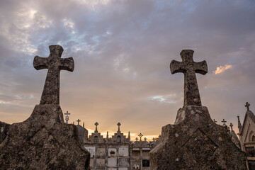 Stone crosses silhouetted against a dramatic sunset sky in a cemetery.