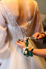 The bride's friends lace up the corset of her wedding dress, helping her get dressed.