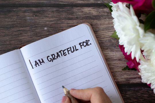 I am grateful handwritten text in notebook on wooden table with flowers. Top view. Thanksgiving and gratitude concept.