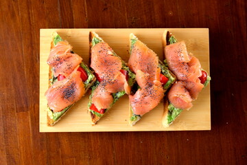 Tramezzini al salmone affumicato serviti su tagliere in legno, tagliati a triangolo. Eleganti e gustosi, perfetti per aperitivi o buffet. Fotografia realizzata con vista dall&rsquo;alto.