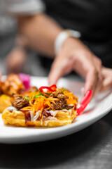 Close-up of gourmet waffles topped with shredded meat, vegetables, and sauce, served on a white plate, showcasing elegant food styling and culinary presentation.