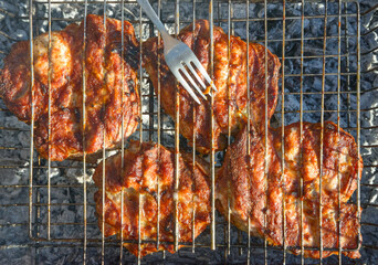 Closeup four pieces of pork neck browned on outdoor grill.