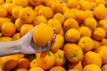 Close up asian woman shopper chooses fresh organic oranges from a large pile of oranges in at supermarket. Shopping concept