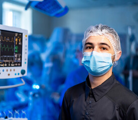 Surgical medical professional. A healthcare worker wearing a mask and cap stands in a busy surgical...